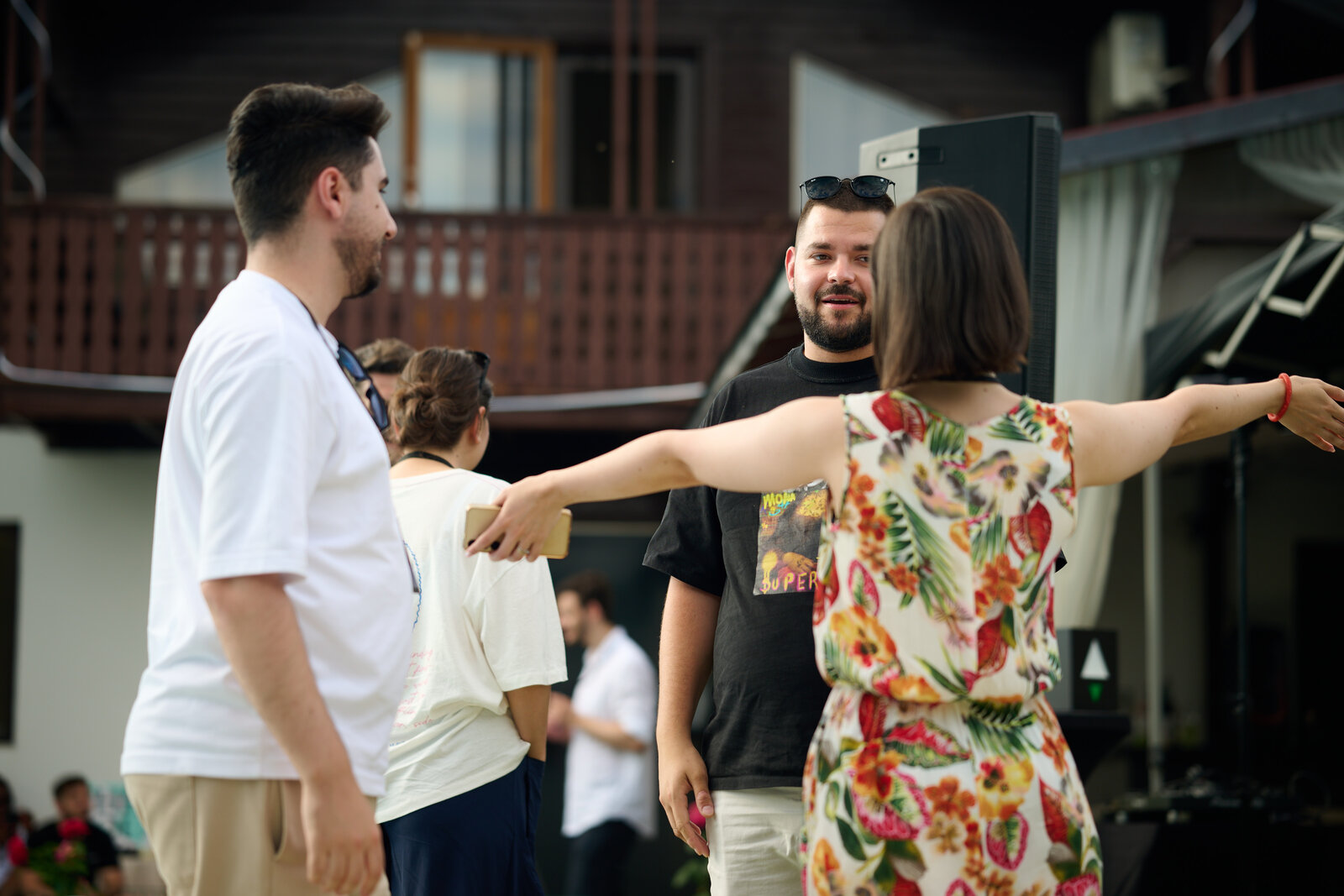 Doi participanți salutându-se în fața casei, unul cu brațele larg deschise