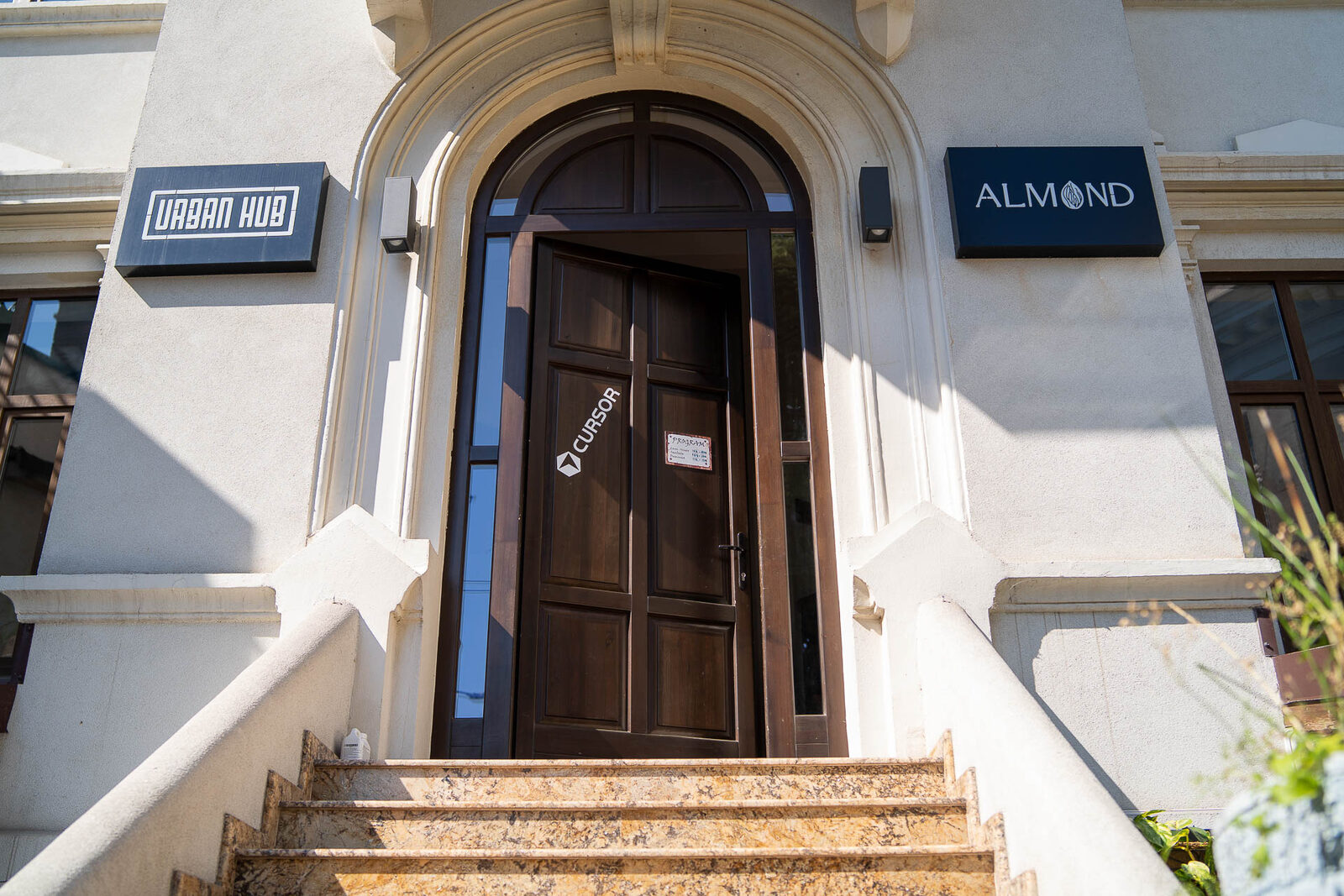 The arched wooden front door of Urban Hub in Bucharest, a Cursor sticker stuck to it, under the venue sign.